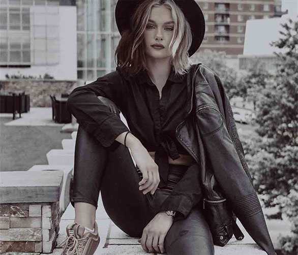 Web Developer wearing a hat, sitting on steps of an office building with a leather jacket over her shoulder.