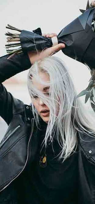 Woman wearing black leather jacket holding flowers above her head.