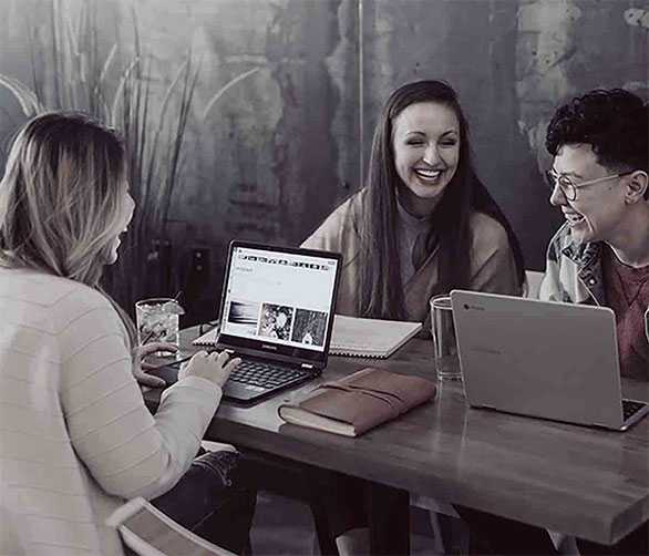 Web Developers are sitting at a table with their laptops smiling, discussing website development.